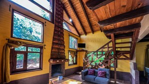 Ein gemütliches Zimmer mit einer Holztreppe, einem Kamin und großen Fenstern mit Blick auf Grünflächen.