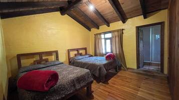 A room with two beds, wooden flooring, a sloped ceiling, and a door leading to a balcony.
