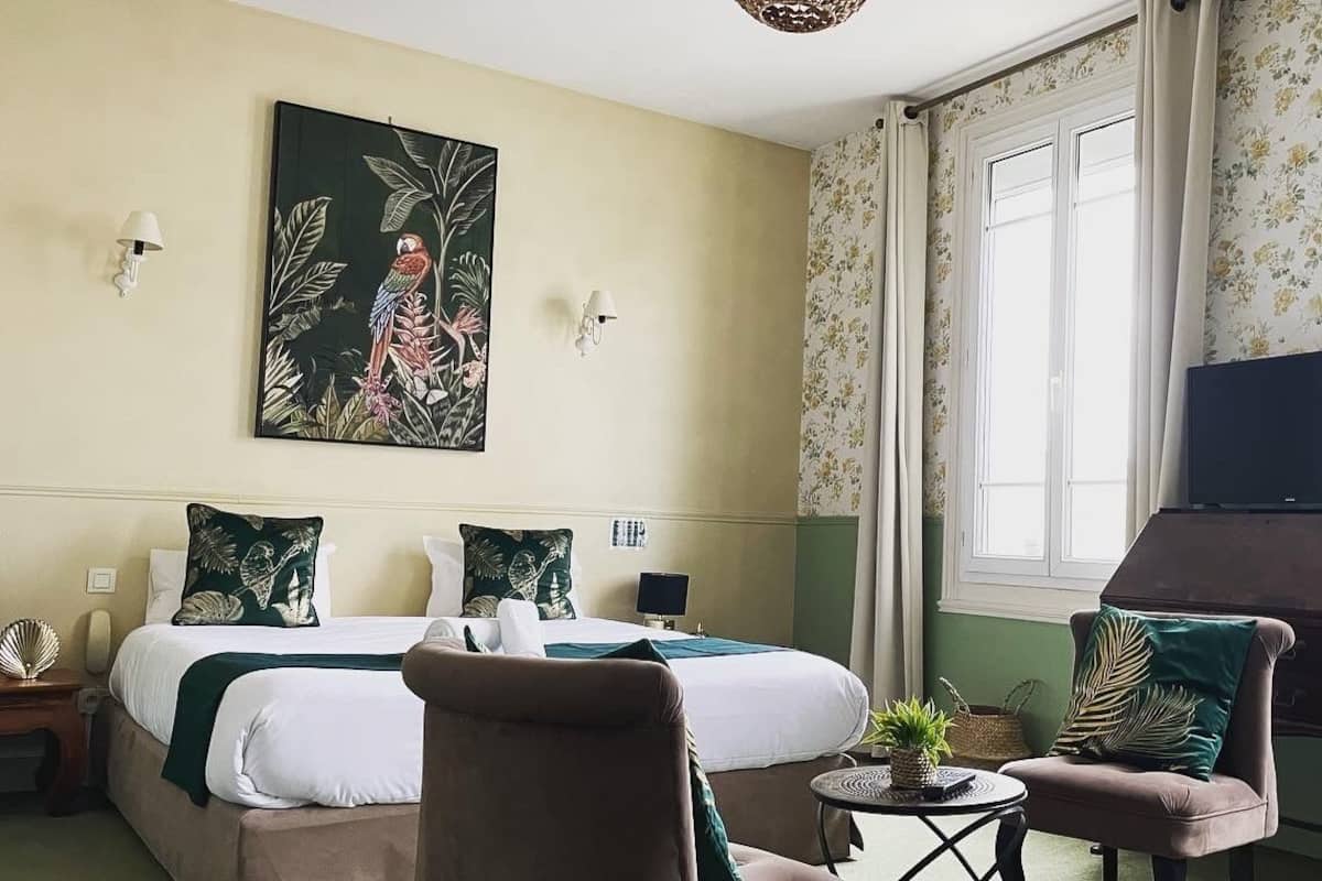 Ein Hotelzimmer mit einem Bett, einem Sessel, einem kleinen Tisch mit Pflanze und einem Bild an der Wand.