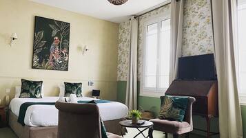 A hotel room with a bed, a chair, a small table with a plant, and a painting on the wall.