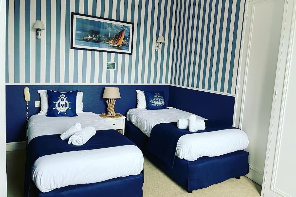 Ein Hotelzimmer mit zwei Betten, gestreifter Tapete, einem gerahmten Bild eines Segelbootes und einem Telefon auf dem Nachttisch.