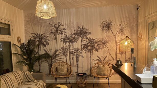 A cozy living room with a sofa, two wicker chairs, a coffee table, and a mural of palm trees. - Hôtel de la Côte Fleurie (Deauville)