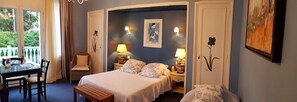 Ein Schlafzimmer mit einem Bett, zwei Nachttischen mit Lampen, einem Sessel, einem kleinen Tisch und einem Bild an der Wand.