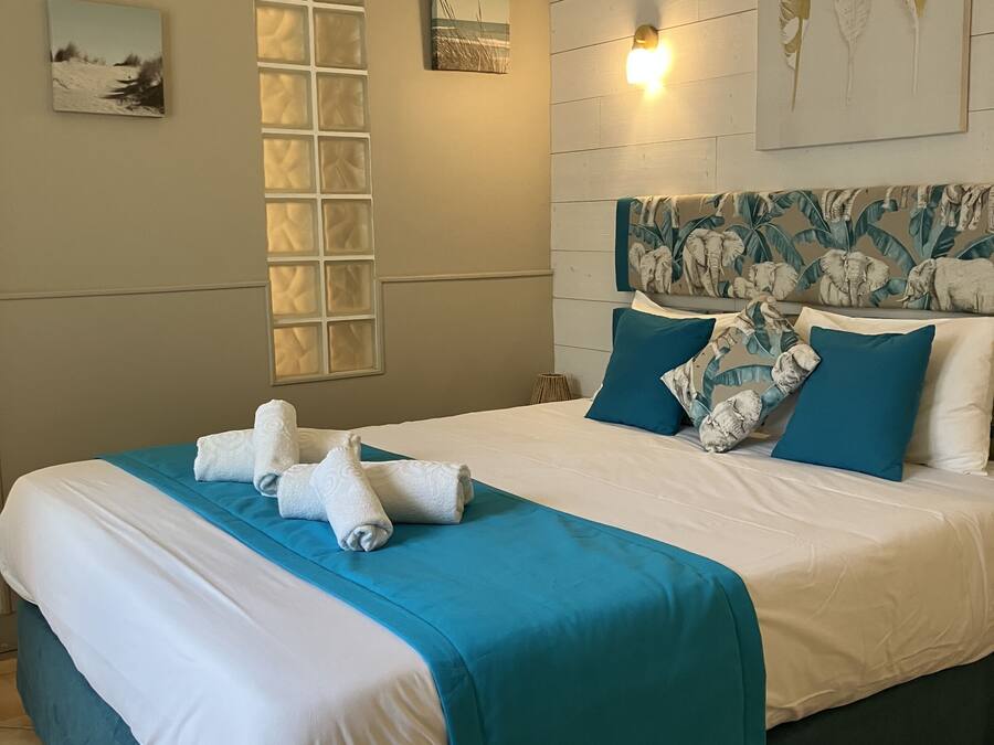 A neatly made bed with a teal and white bedspread, two pillows, and folded towels on a headboard with a leaf pattern.