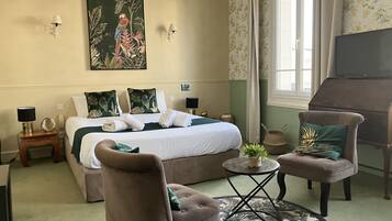 Una habitación de hotel con una cama, dos sillones, una mesita redonda, un piano y un cuadro grande en la pared.