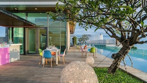 An outdoor dining area with tables and chairs, a pool, and a view of the city skyline.
