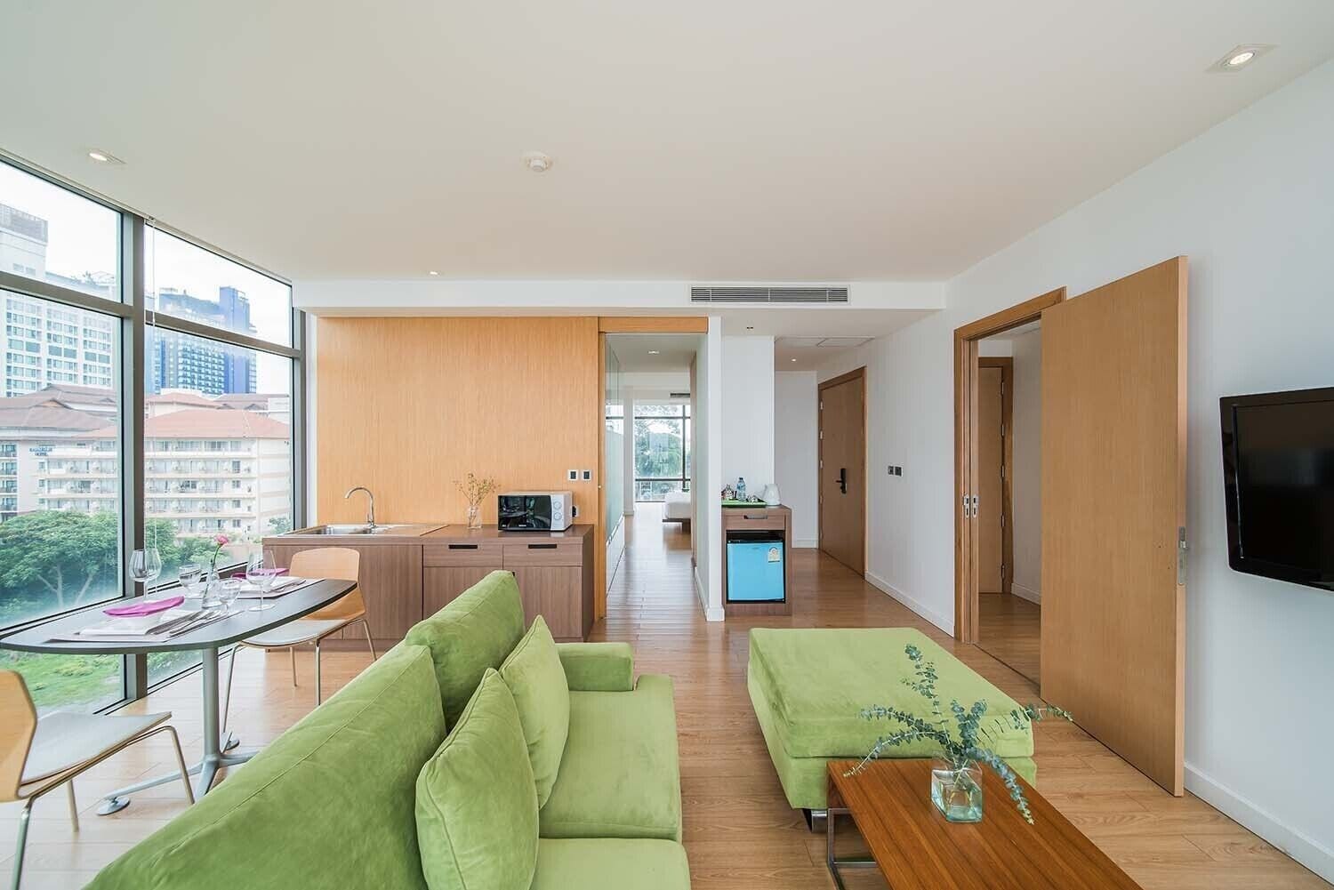 Un appartement moderne comprenant un coin repas, un salon avec des canapés verts, une cuisine et un téléviseur fixé au mur.