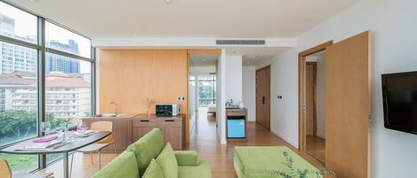 Un appartement moderne comprenant un coin repas, un salon avec des canapés verts, une cuisine et un téléviseur fixé au mur.