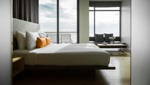 A modern hotel room with a large bed, a view of the sea, and a balcony with a chair.