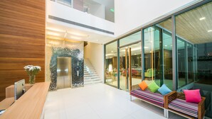 A modern reception area with a wooden desk, a bench with colorful cushions, and a glass wall offering a view of the interior.