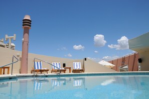 A swimming pool with lounge chairs and umbrellas, a tall column, and a clear blue sky. - InterTower Hotel (Santa Fe)