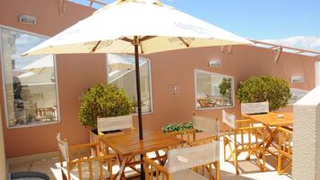 An outdoor patio with wooden tables and chairs, a large umbrella, and potted plants.