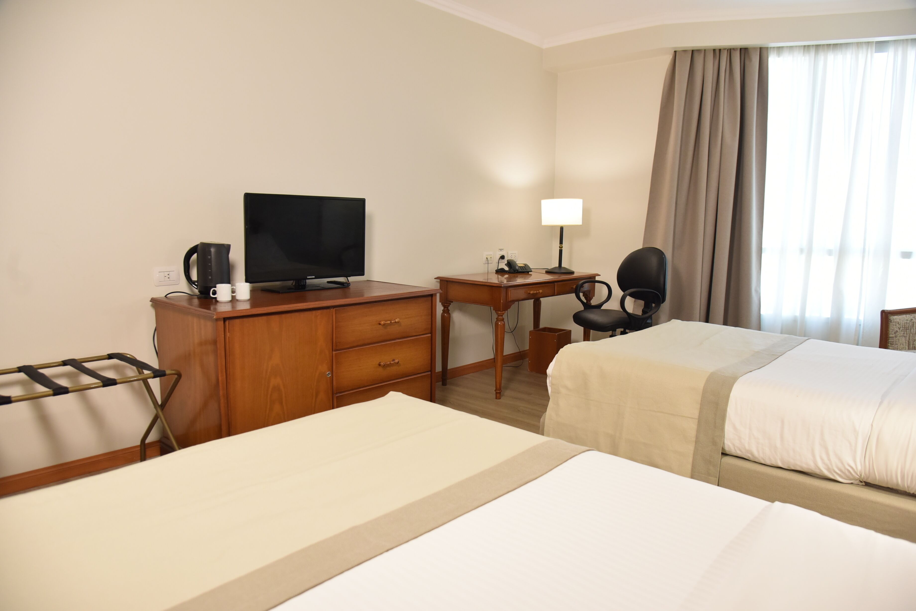 A hotel room with two beds, a desk with a television, a lamp, and a chair.