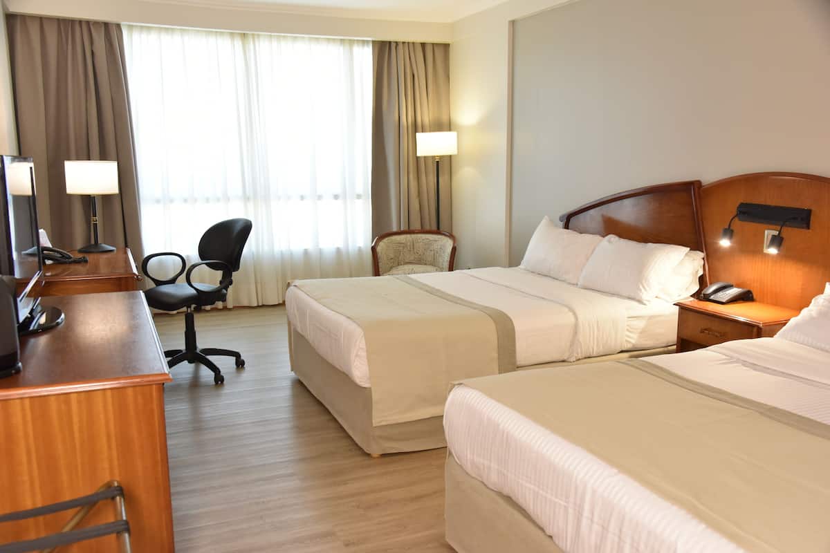 A hotel room with two beds, a desk with a telephone, a chair, and a lamp.