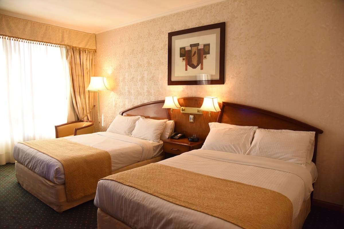 A hotel room with two beds, a nightstand, a lamp, and a framed picture on the wall.