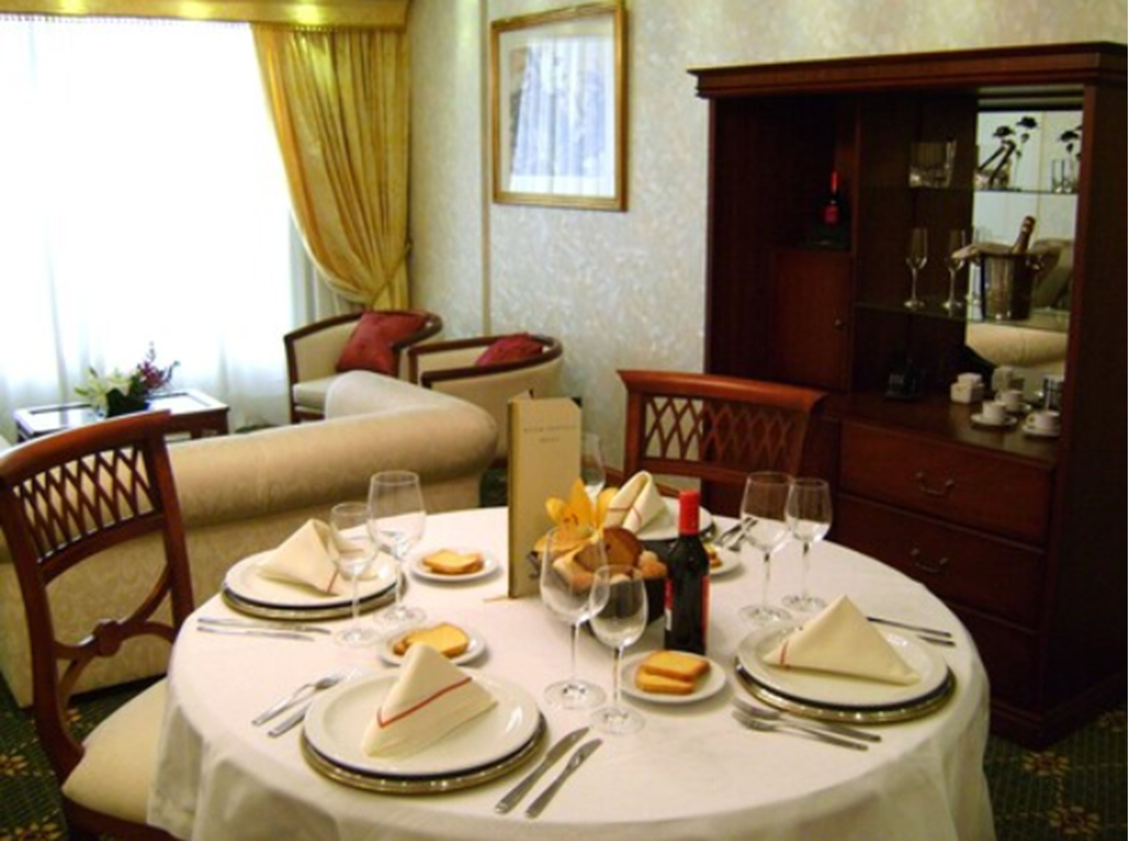 A dining area with a round table set for four, including plates, cutlery, and glasses. There are chairs around the table, and a sofa and armchair in the background.