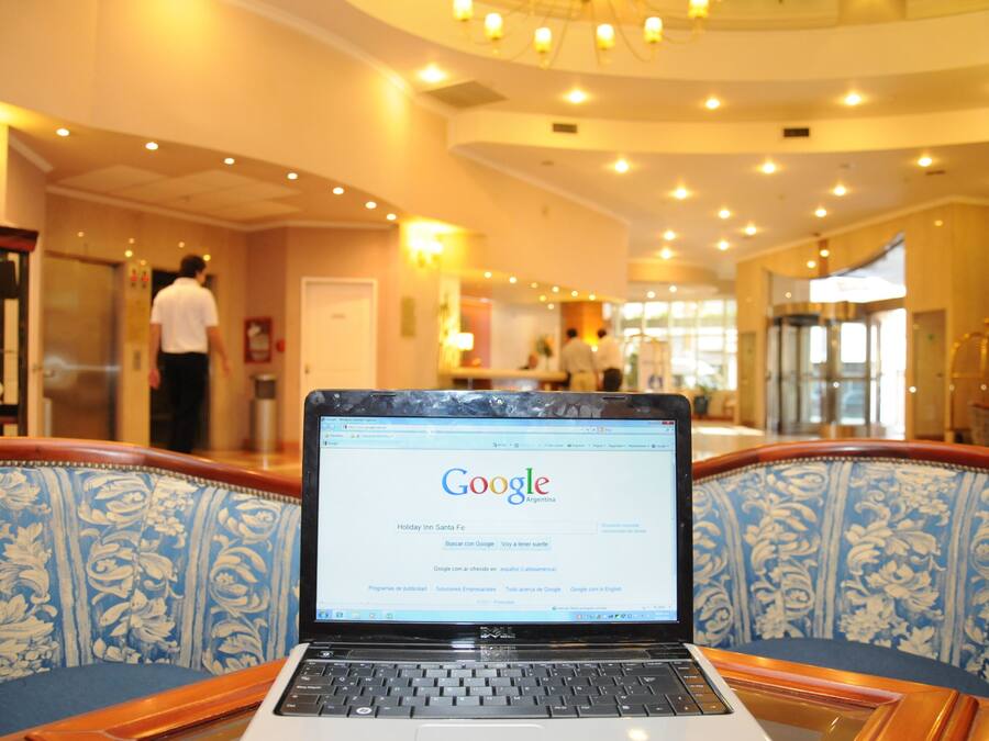 A laptop on a patterned chair in a hotel lobby with a chandelier and a glass elevator in the background.