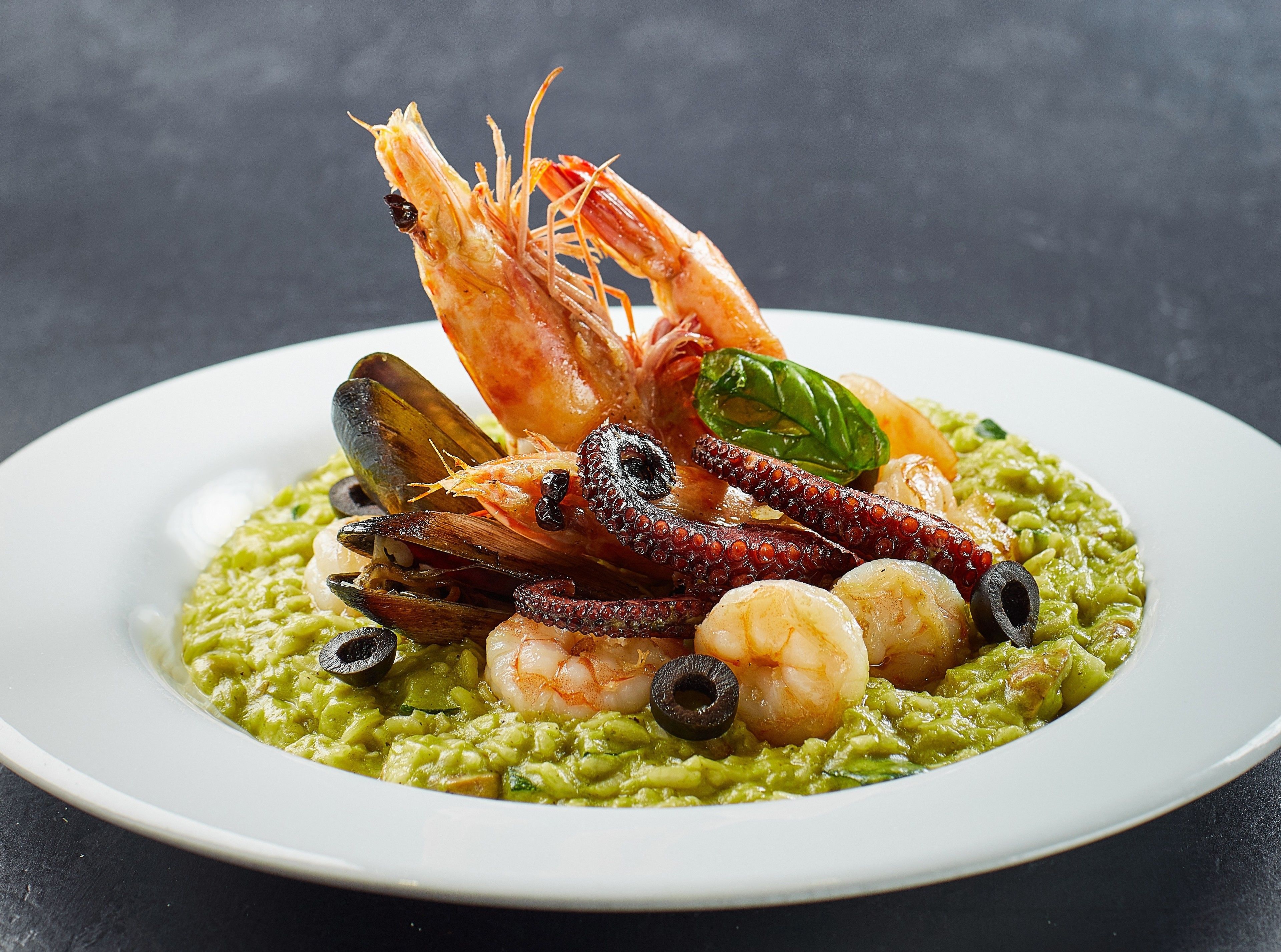 A seafood dish with shrimp, mussels, and octopus on a bed of green sauce.