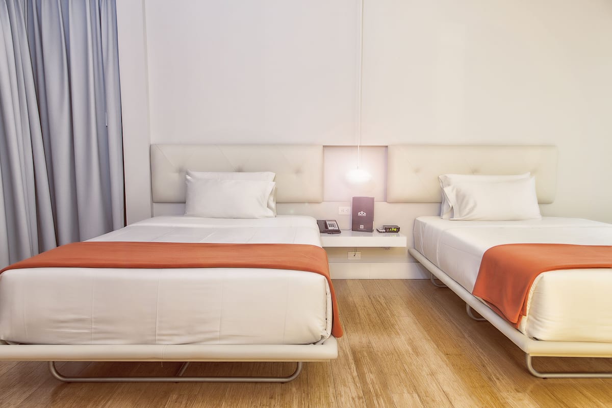A hotel room with two beds, a bedside table with a lamp, and a curtain.