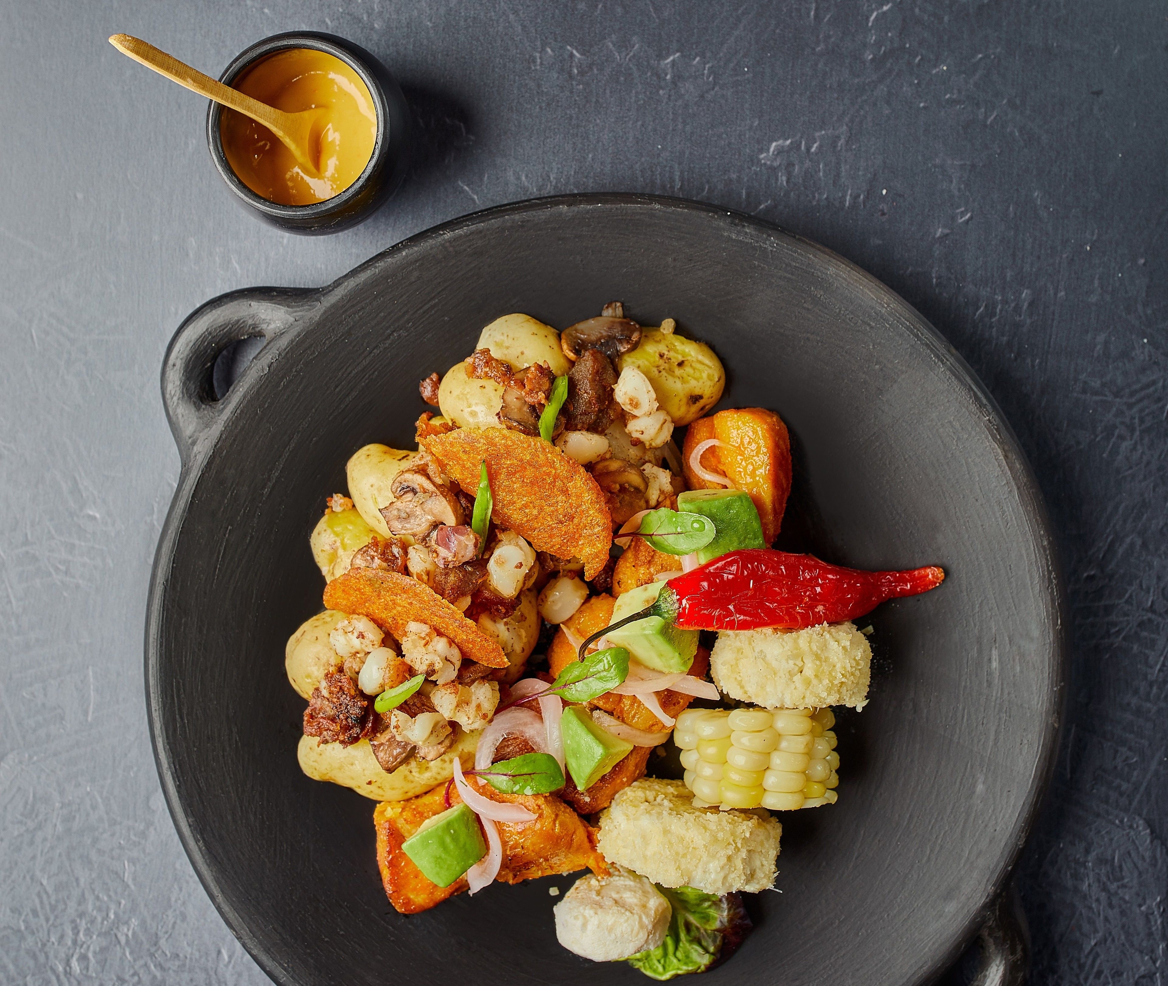 A black plate with a variety of food items including potatoes, corn, and red chili peppers.