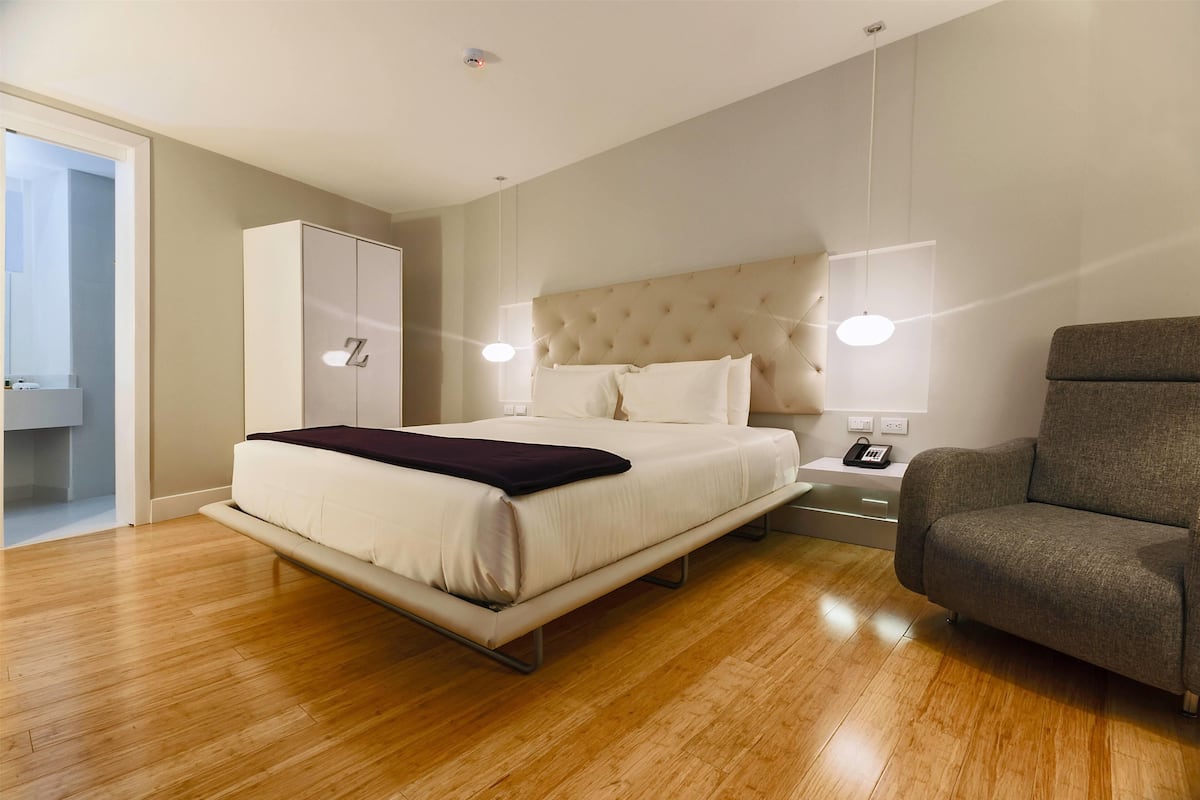 A modern bedroom with a bed, a wardrobe, a sofa, and a bedside table with a lamp.