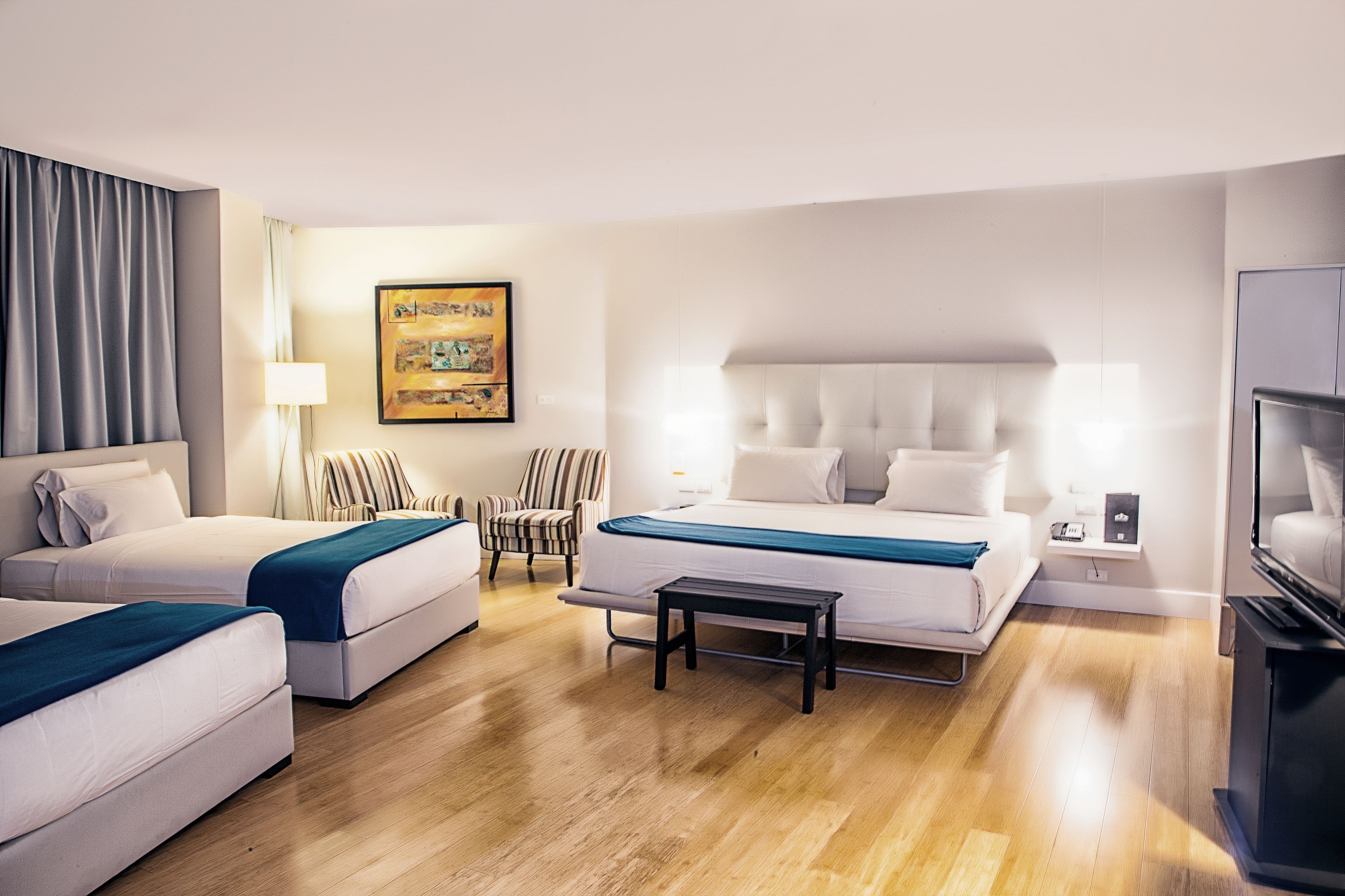 Une chambre d’hôtel avec deux lits, un canapé, une petite table, une télévision et un tableau au mur.