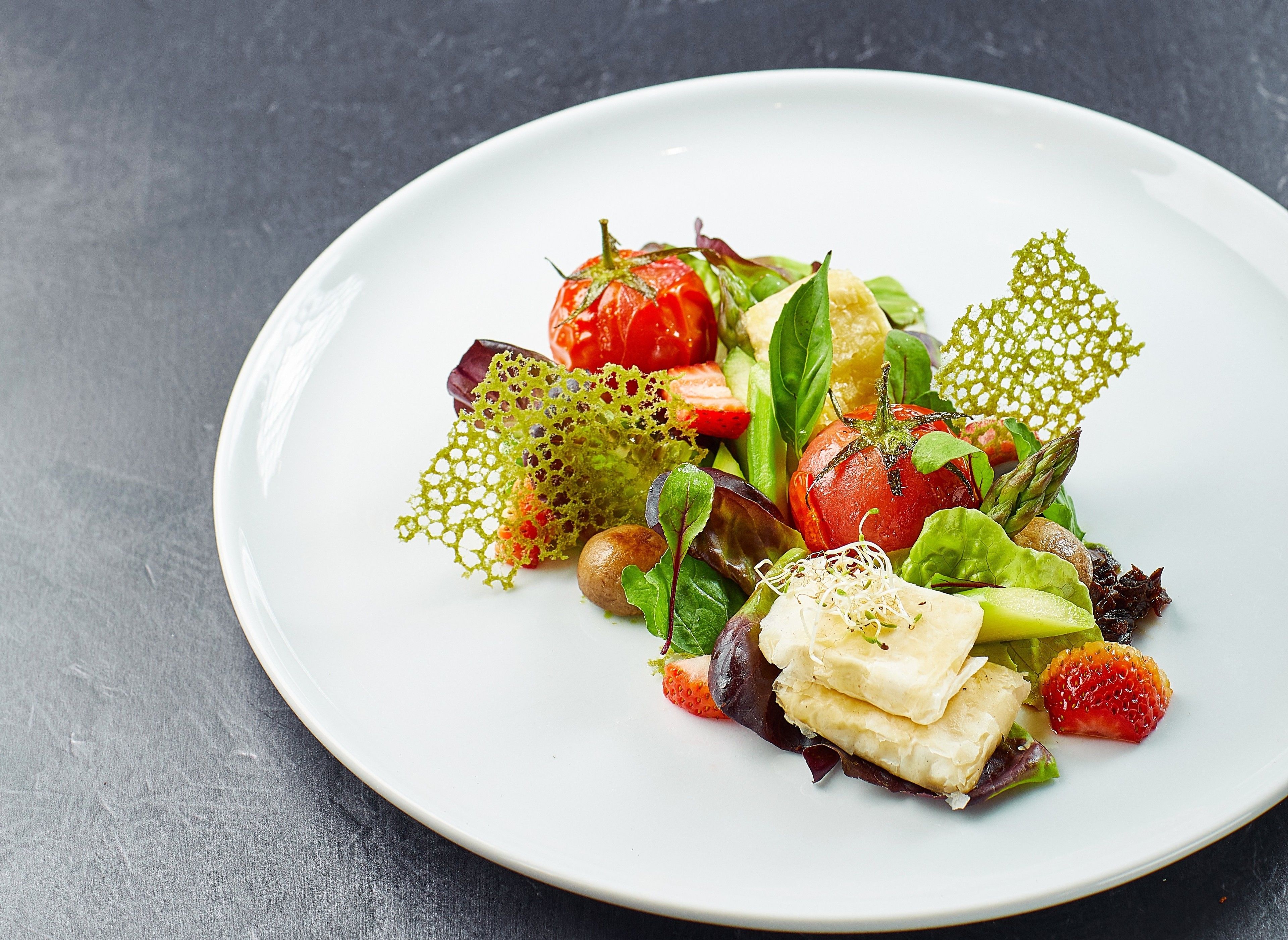 A white plate with a salad containing tomatoes, lettuce, and other greens.