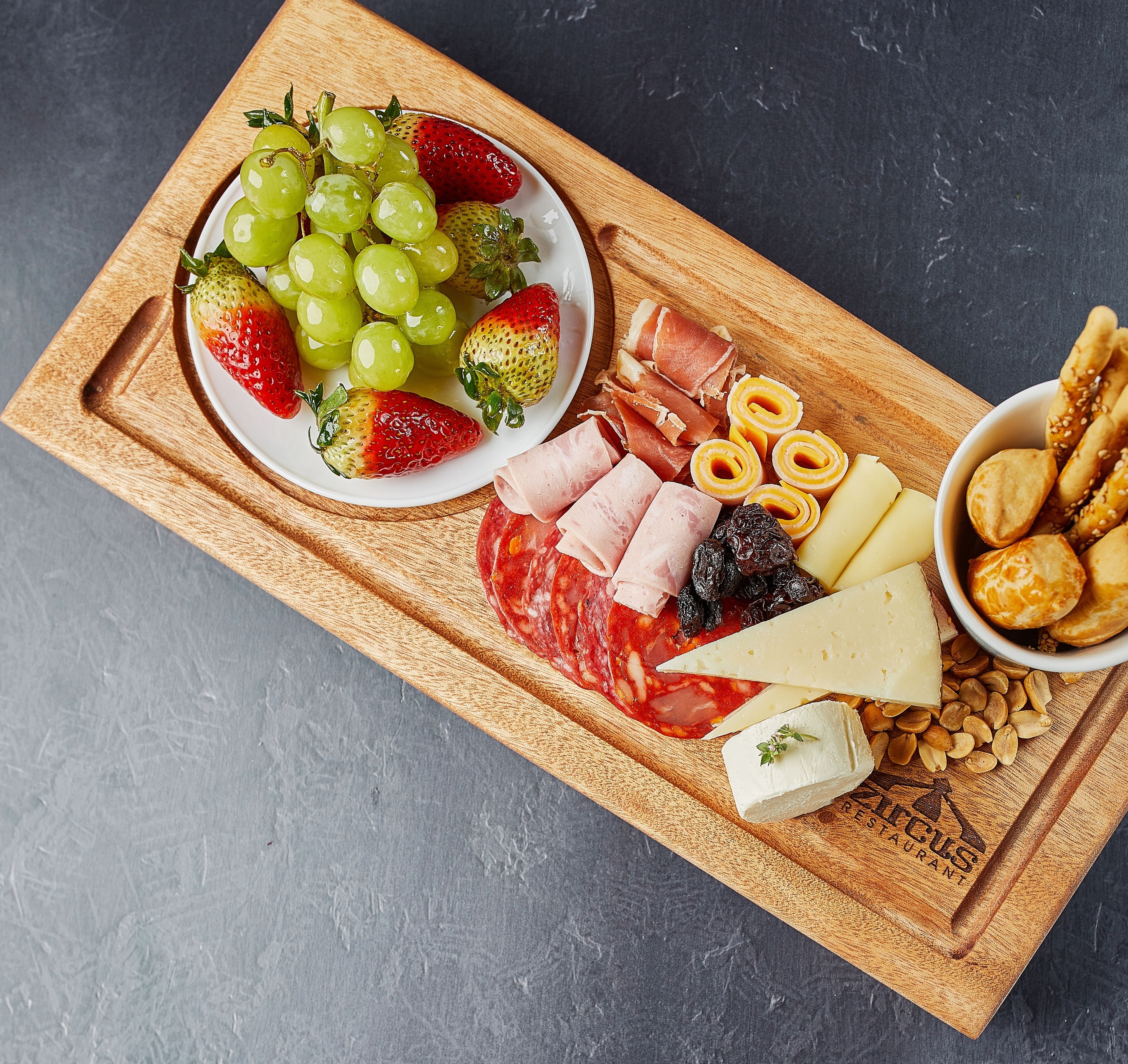 Ein Holzbrett mit einer Auswahl an Käse, Wurstwaren und Früchten.