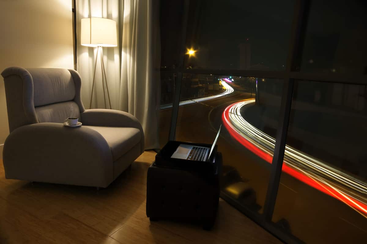 A modern room with a laptop on a small table, a chair, and a view of a city street at night.
