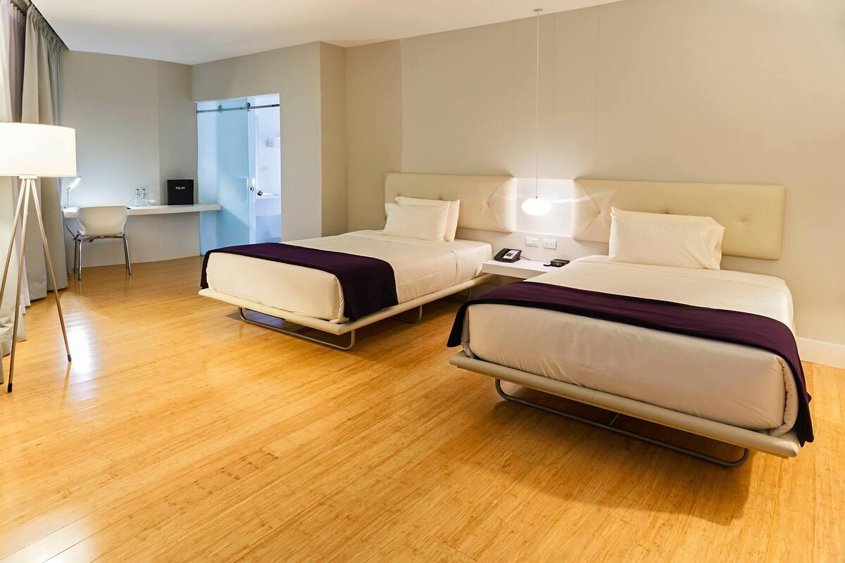 A hotel room with two beds, a desk, a chair, and a wardrobe.
