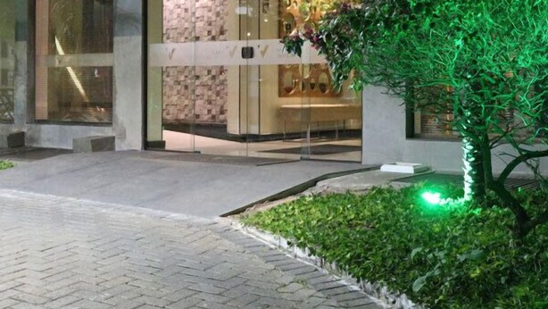 A hotel entrance with a glass facade, a brick pathway, and a small garden area with a palm tree. - Vida Plaza Hotel (Nucleo Bandeirante)