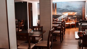 A restaurant with wooden tables and chairs, a view of a cityscape through a large window, and a modern interior design. - Vida Plaza Hotel (Nucleo Bandeirante)