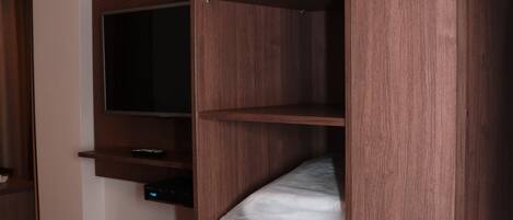 Une pièce dotée d’une bibliothèque intégrée en bois, d’un téléviseur à écran plat fixé au mur et d’un petit bureau avec un téléphone.