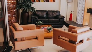 A modern living room with a black leather sofa, two brown leather armchairs, a wooden coffee table with a plant, and a bookshelf with books and decorative items. - Vida Plaza Hotel (Nucleo Bandeirante)