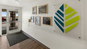 Ein Flur mit gerahmten Bildern an der Wand, einer Glastür und einem großen, abstrakten Logo.