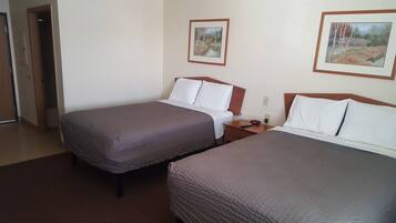 A hotel room with two single beds, a wooden nightstand, a remote control, and two framed pictures on the wall.
