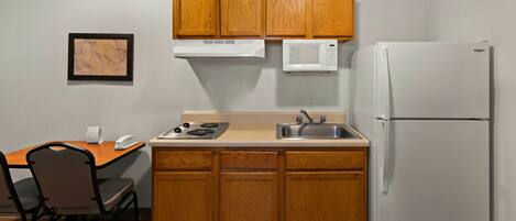 A compact kitchen with wooden cabinets, a microwave, a stove, a sink, and a refrigerator.