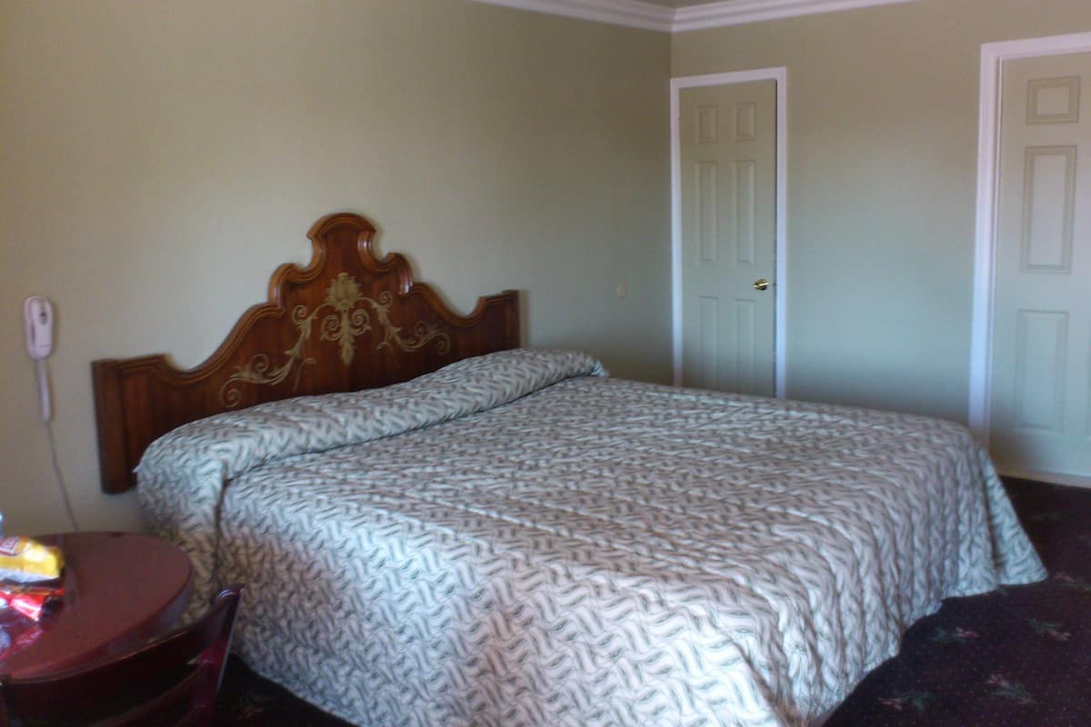 A bedroom with a wooden headboard, a patterned bedspread, a bedside table with a lamp, and a door.