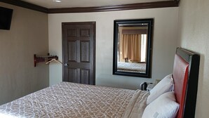 Quarto de hotel com cama, porta, espelho e cabideiro.