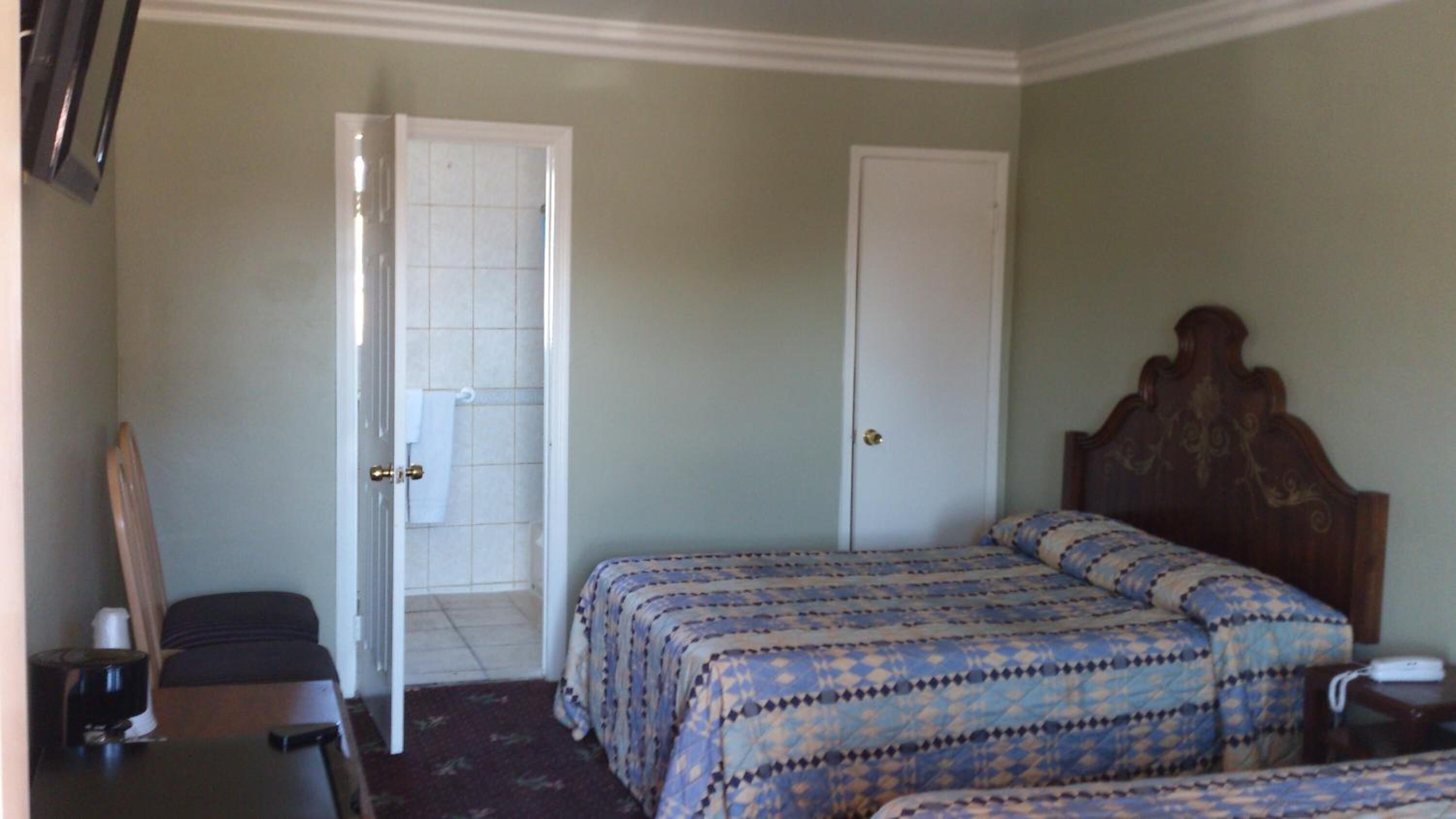 A room with two beds, a chair, a desk, and a door leading to a bathroom.
