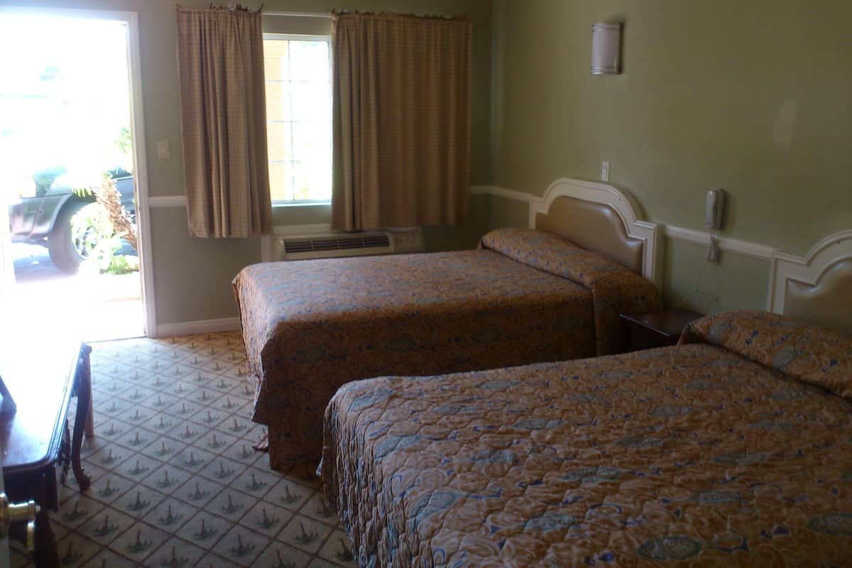 A hotel room with two beds, a window with curtains, a radiator, and a small table.