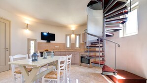 Una cocina moderna con comedor, televisor sobre la encimera y una escalera en espiral que sube a un nivel superior.