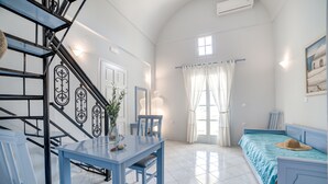 Una habitación con escalera, una mesa de comedor con sillas, una cama con colcha azul y una ventana con cortinas.