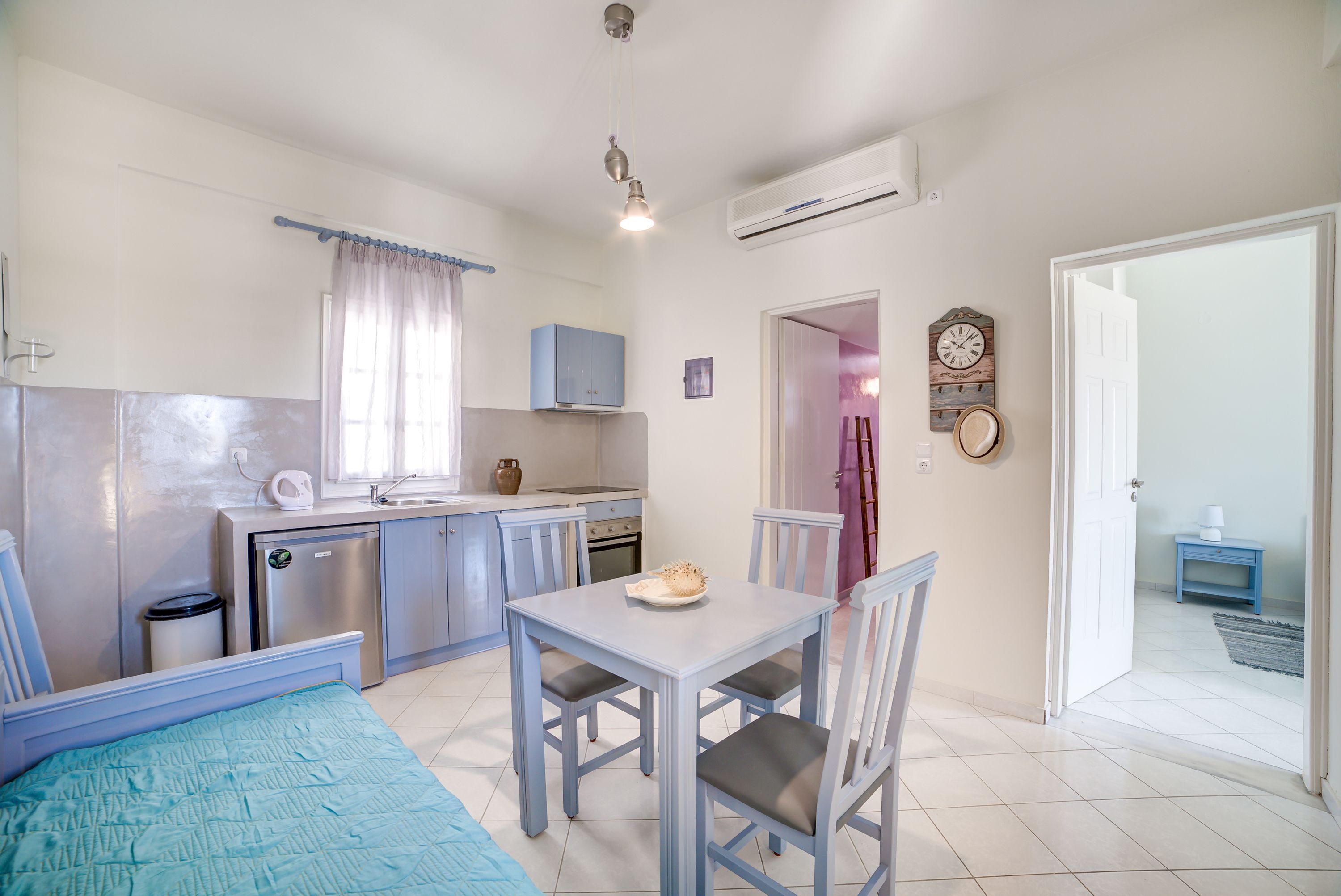Une cuisine compacte comprenant une table et des chaises, un petit réfrigérateur et une fenêtre avec des rideaux.