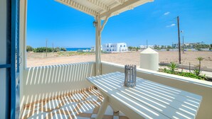 Un espacio al aire libre techado con una mesa y sillas, vista a la playa y un cielo azul despejado.