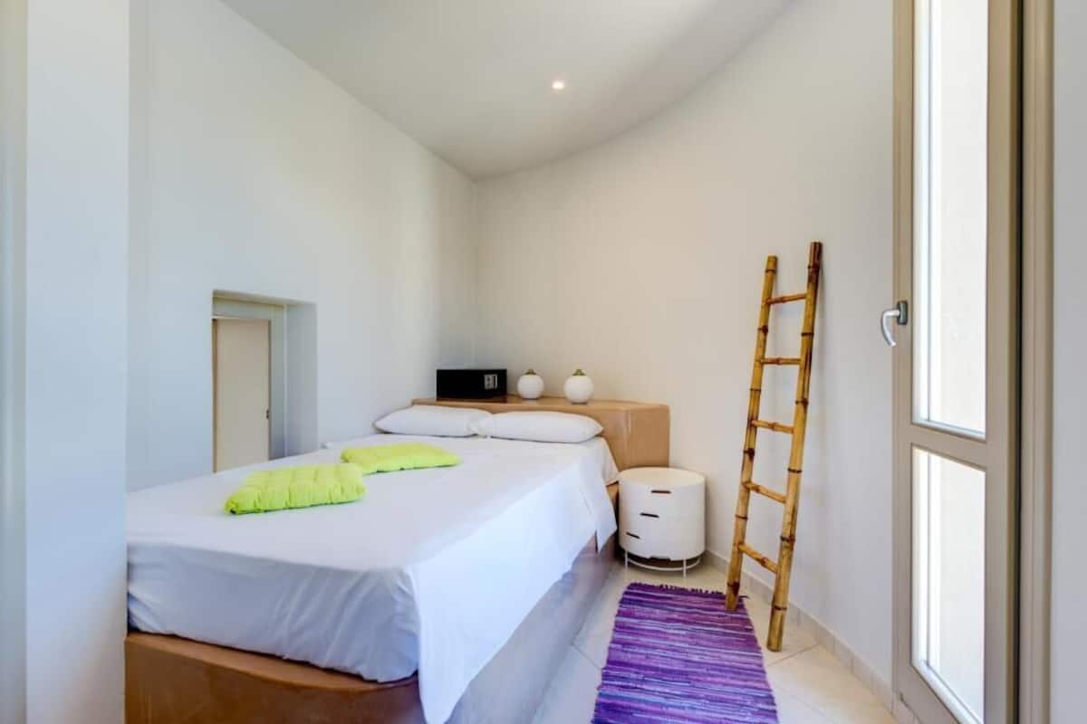 A modern bedroom with a bed, bedside tables, a ladder, and a window.