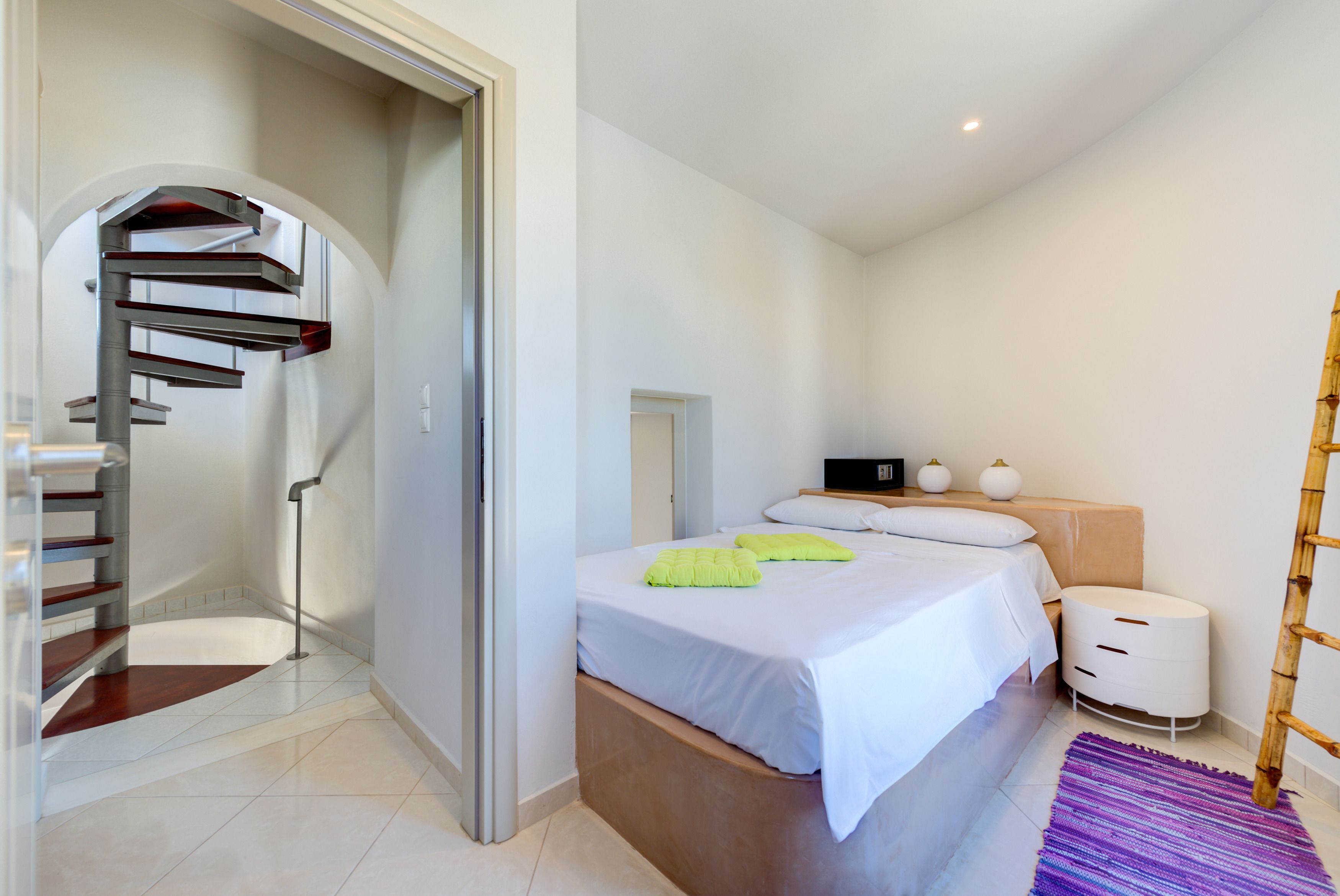 Une chambre à coucher comprenant un lit, une table de chevet, une lampe et un escalier menant à une autre pièce.