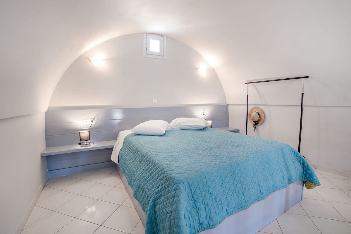 A bedroom with a bed, bedside table, lamp, and a small window.