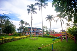 A playground with slides and swings, surrounded by well-maintained grass and palm trees. - Finca Hotel La Tata (Montenegro)