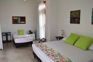 Habitación de hotel con dos camas, una mesita pequeña, una silla, un escritorio y una ventana con cortinas.